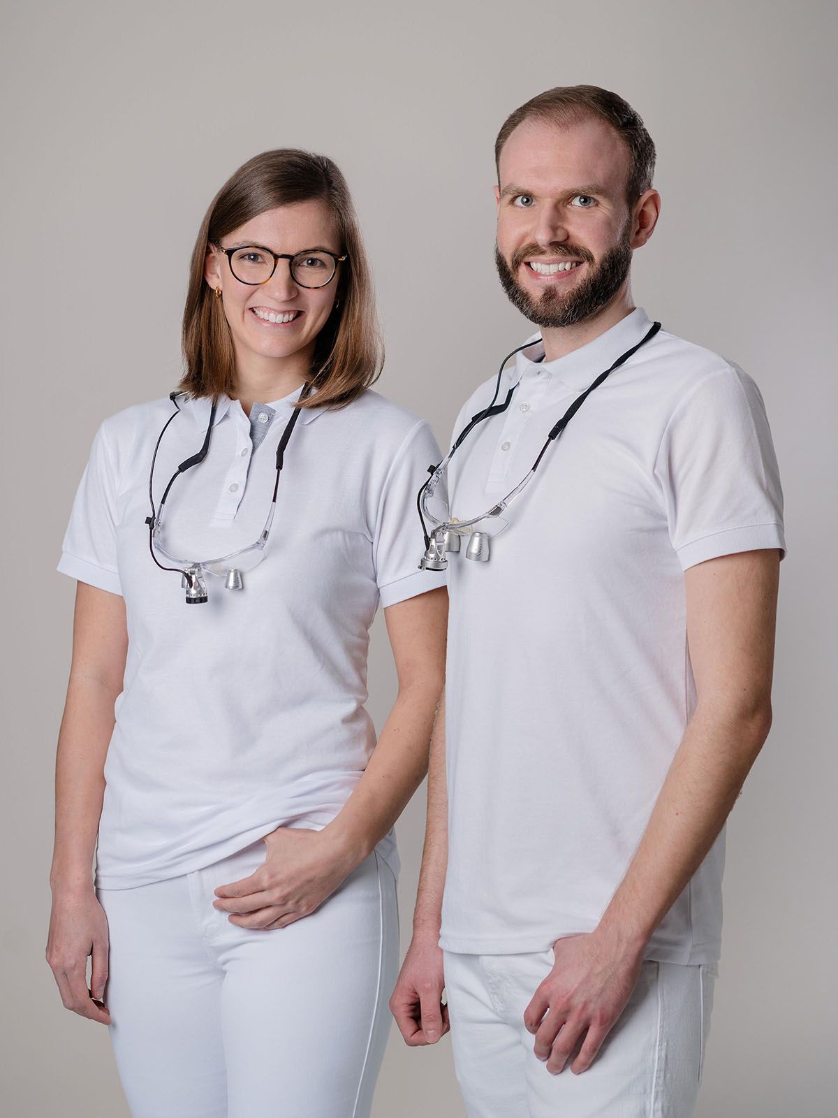 Porträt von Dr. Verena Gernart und Dr. Marvin Gernart, die nebeneinander vor schlichter weißer Wand stehen