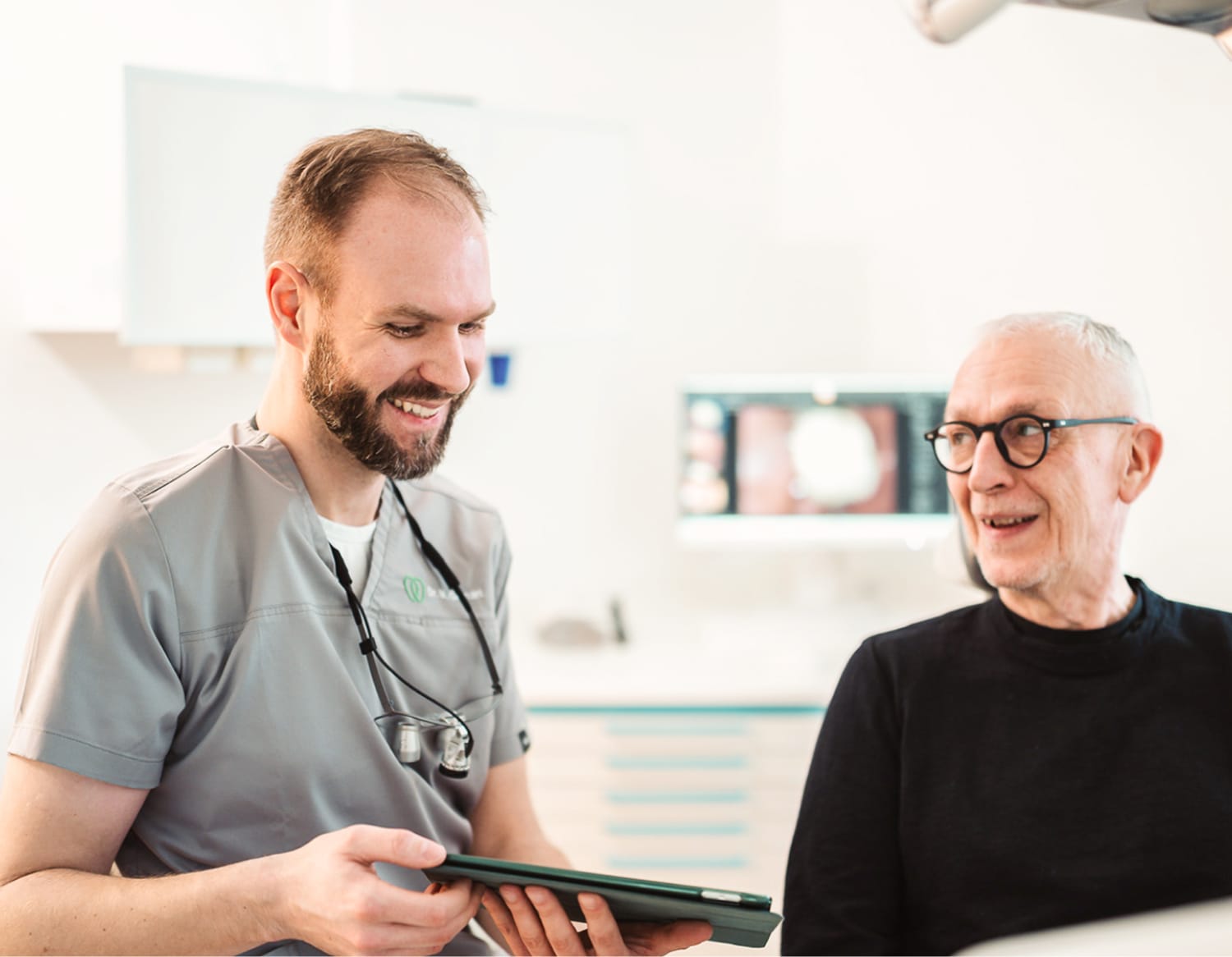Dr. Marvin Gernart erklärt einem Patienten etwas auf dem iPad in freundlicher Atmosphäre